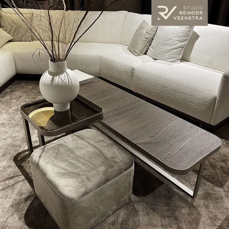 Zithoek met witte bouclé hoekbank, houten salontafel op bronskleurig frame, velours poef en sculpturale vaas met droogtakken.