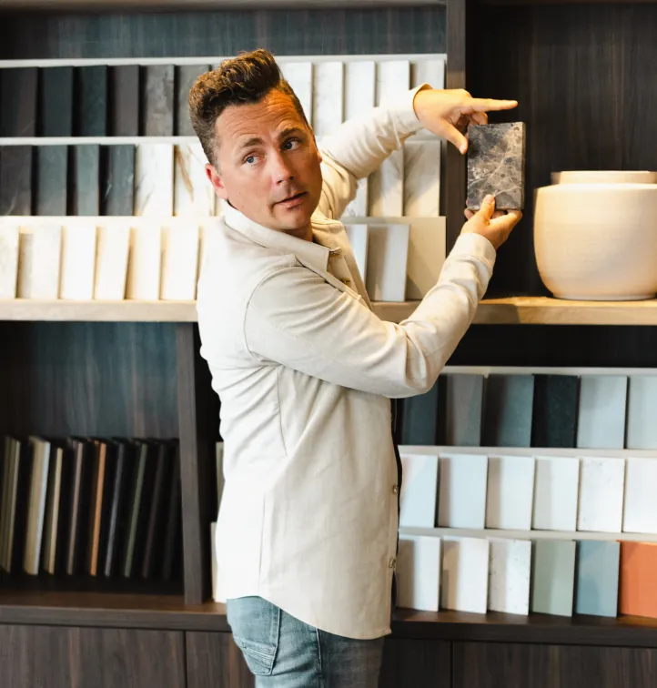 Reinder Veenstra houdt een marmerstaal omhoog bij de materialenwand met kleur- en steenmonsters in de studio.